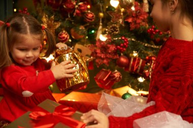 Küçük bir kız uçan bir hediye yakalıyor gülümsüyor ve Noel 'i ve bayramı bekliyor rahat bir ev, yanan bir şömine ve bir Noel ağacı.