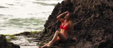 Parlak mayo giymiş güzel bir kız Bali Adası 'nda kayalar ve okyanuslarla seksi pozlar veriyor.