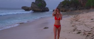 Güzel, seksi bir kız gün batımında sahilde yürüyor. Çok parlak, sıcak bir güneş ve kumsalda beyaz bir kumla. Okyanusta bazı sörfçüler dalgalarını alıyor.