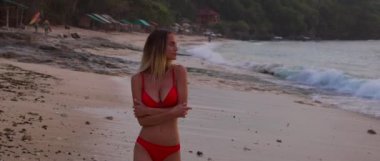 Güzel, seksi bir kız gün batımında sahilde yürüyor. Çok parlak, sıcak bir güneş ve kumsalda beyaz bir kumla. Okyanusta bazı sörfçüler dalgalarını alıyor.