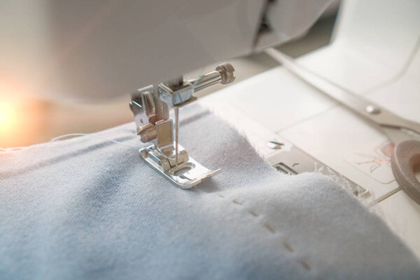 Швейная машинка и предмет синей одежды. Крупный план шитья юбок. Игла швейной машинки застряла в голубой ткани и ножницы рядом
