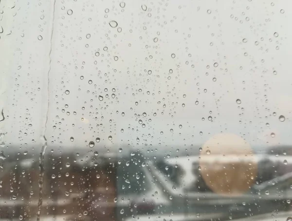 Pencereye yağmur damlaları, trafik ışıkları, şehirde yağmurlu bir sabah, soyut bir arka plan.