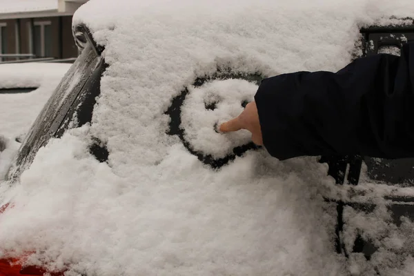 A man draws a smiley on the snow covering side window of the car with his finger