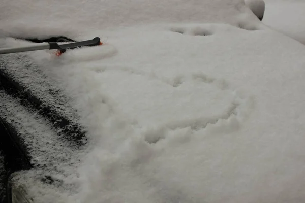 Heart drawn on the snow covering the hood of the car. Man cleaning snow on the hood of the car with brush
