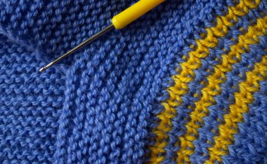 Blue knitted pattern with yellow threads. Metal crochet hook with yellow tip. Knitting and crocheting. Creativity and Hobbies.