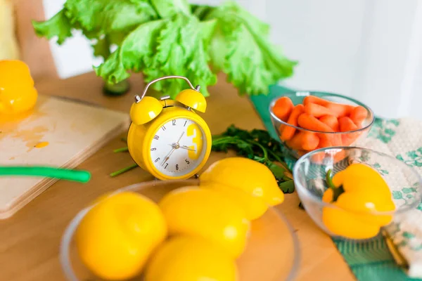 Yellow cooking timer between fresh cooking ingredients - vegetables, lemons and green salad