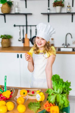 Sevimli küçük kız beyaz mutfakta renkli sebzelerden salata hazırlıyor..