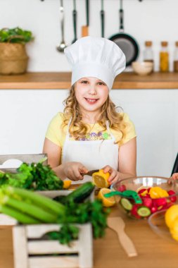 10 yaşındaki güzel, gülümseyen bir kız kesinlikle sarı taze bir limon keser ve masadaki beyaz, modern bir mutfakta salata hazırlar.