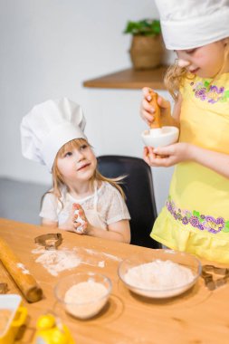 Evde aile sahnesi. İki tatlı kız kardeş mutlu bir şekilde kurabiye ve çörek pişiriyor.