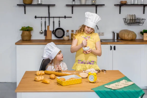 Evde aile sahnesi. İki tatlı kız kardeş mutlu bir şekilde kurabiye ve çörek pişiriyor.