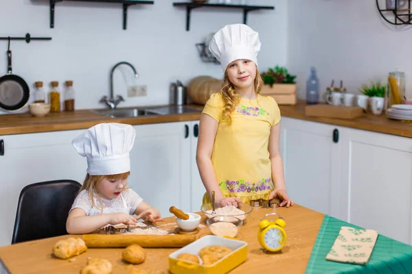 Evde aile sahnesi. İki tatlı kız kardeş mutlu bir şekilde kurabiye ve çörek pişiriyor.