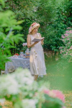 Çiçekli şapkalı ve retro elbiseli güzel bir kız bir kır evinin bahçesinde dinleniyor. Yeşil ve pembe şekerlemelerle çevrili cam bir tabakta kırmızı olgun çileklerin olduğu bir masada otururken, bir yudum su ve şakayık... 