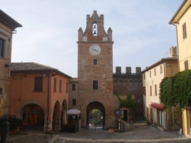 Gradara köyünün tarihi merkezinde arka planda saat kulesi olan binalardan geçen bir sokak.