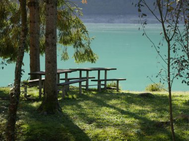 Barcis Gölü - gölün turkuaz suyundaki çimlerin üzerinde piknik masası