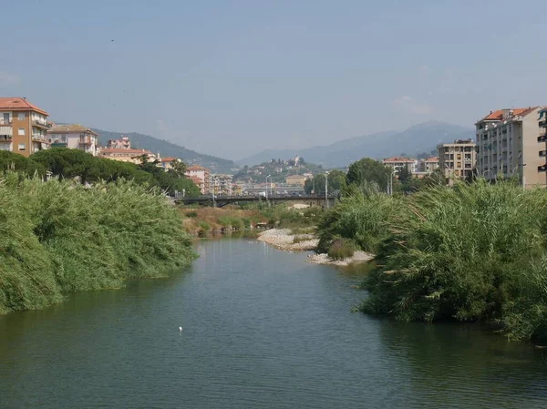 インペリア ポルト マウリツィオをインペリア オネグリアから木の並ぶ川岸と橋で隔てるインペリア トレント — ストック写真