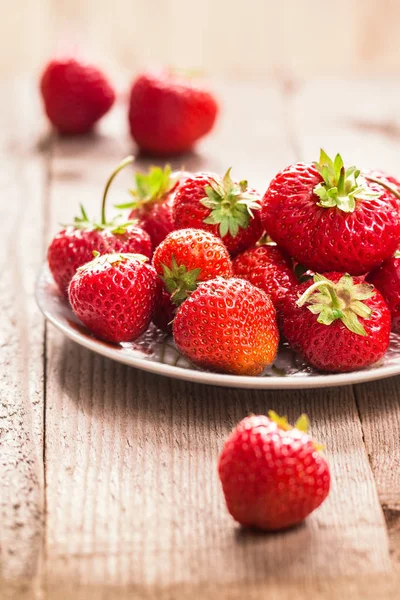 Reife Erdbeeren auf weißem Teller, auf Holztisch — Stockfoto