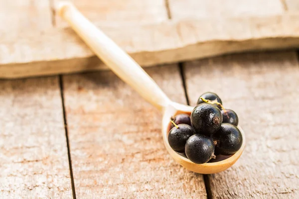 Black currant in wooden spoons on wooden background — Stock Photo, Image