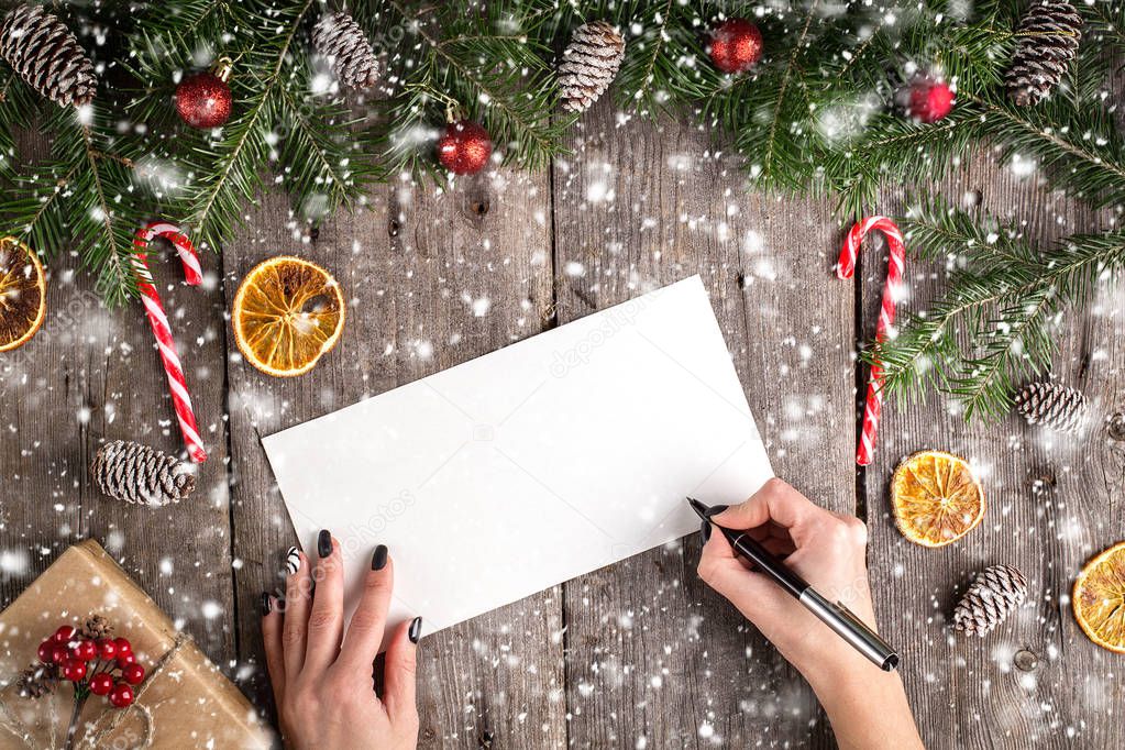 Female hand writing a letter to Santa on wooden background