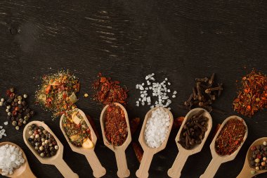 Koyu ahşap masa üstünde tahta kaşıklar içinde çeşitli baharatlar