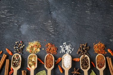 Koyu ahşap masa üstünde tahta kaşıklar içinde çeşitli baharatlar