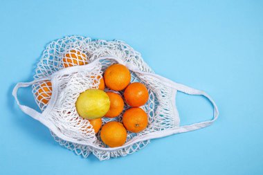 A white cotton string bag with tangerines and lemon lies on a blue background