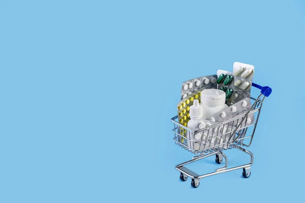 Medizinkonzept. verschiedene Kapseln, Tabletten und Medikamente im Einkaufswagen auf blauem Hintergrund — Stockfoto