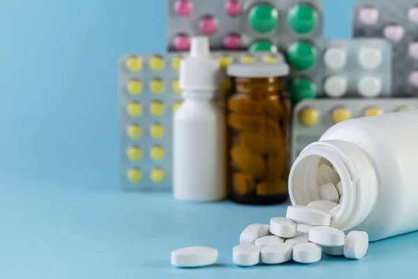 Pills spilling out of white bottle on blue background — Stock Photo, Image