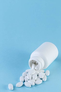 Pills spilling out of white bottle on blue background.