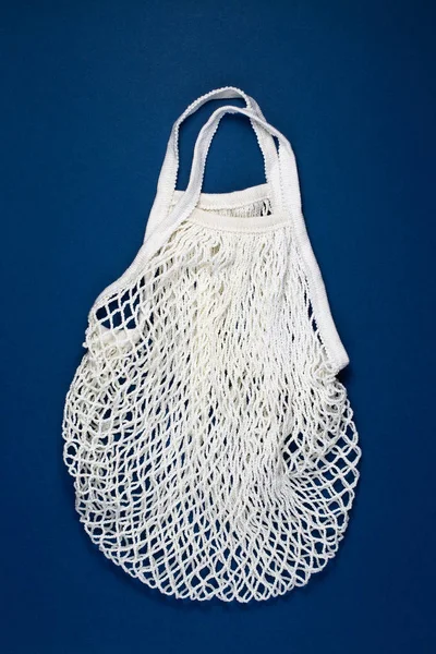 White cotton mesh bag on blue paper background. Top view, flat lay, copy space