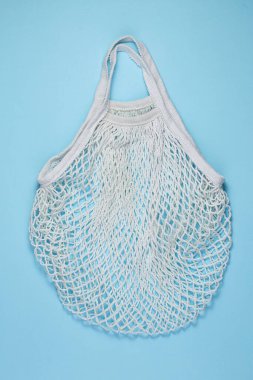 Mavi kağıttan arka planda beyaz pamuklu örgü çanta. Renkli arka planda yeniden kullanılabilir alışveriş torbası. Ekolojik, sıfır atık kavramı. Üst görünüm, düz görünüm, kopyalama alanı