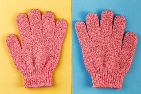 A pair of pink massage gloves for shower on blue and yellow background. Gloves for use in the shower for massage and scrub. Beauty background with cosmetic products. Beauty, health and spa concept