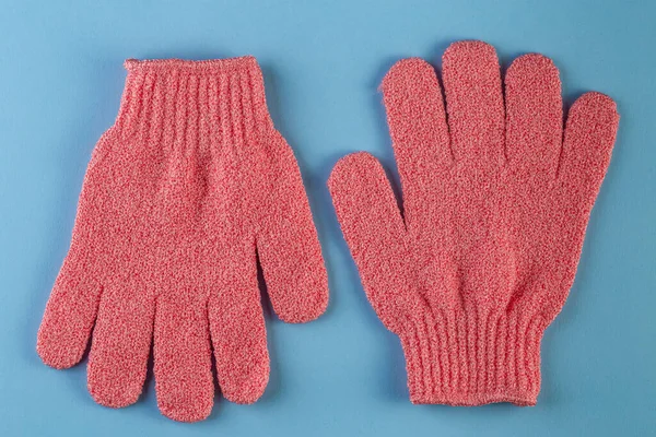 A pair of pink massage gloves for shower on blue background. Gloves for use in the shower for massage and scrub. Beauty background with cosmetic products. Beauty, health and spa concept