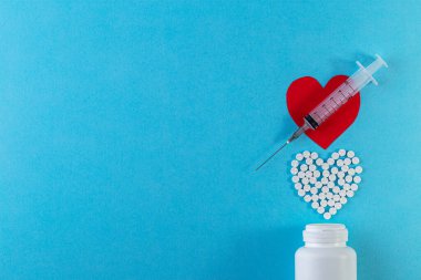 Kalp şeklinde haplar ve mavi arka planda şırınga. İlaç, sağlık için konteynırda tedavi. Tıp konsepti. Üst görünüm, kopyalama alanı olan düz uzanmış