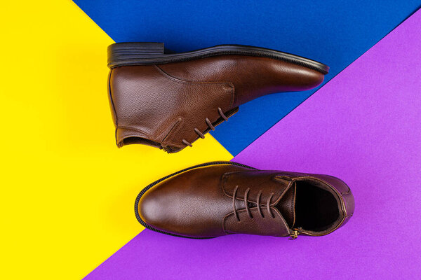 A pair of brown leather boots on color paper background.