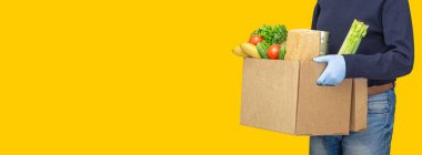 Teslimatçı, tıbbi lastik eldivenlerde karton kutular tutuyor. İnternetten alışveriş ve ekspres teslimat. Yemek dağıtım servisi. Gönüllü bir bağış kutusu dolusu yiyecek getiriyor. Coronavirüs karantinası. 