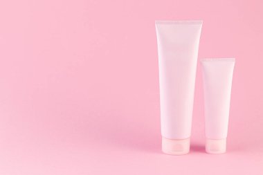 Pastel pembe arka planda iki kozmetik tüp paketi. Boş plastik kaplar, basit ambalaj tasarım şablonu. Sığ alan derinliği, uzay fotoğrafçılığını kopyala. 