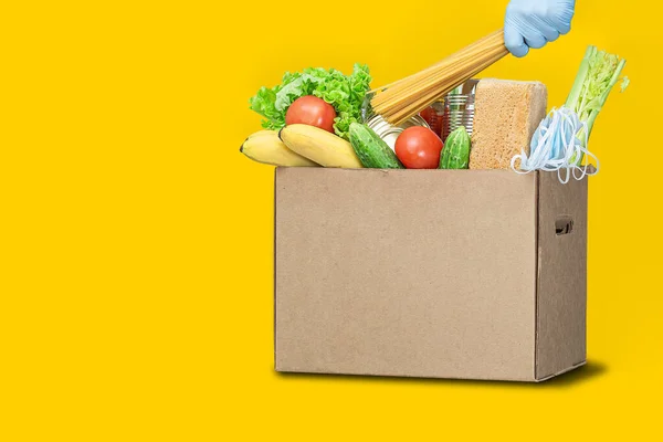 Donation box with food on a yellow background. Coronavirus food delivery. Volunteer brings a box of food. Donation, quarantine concept. Volunteer collecting food. Copyspace.