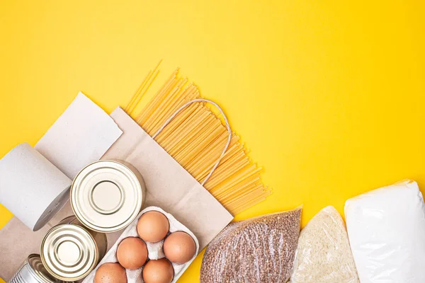 Paper bag with food, canned food, tomatoes, cucumbers, bananas on yellow background. Donation, coronavirus quarantine. Food supplies for quarantine. Food delivery. Copyspace.