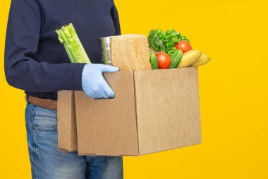 Teslimatçı elinde plastik eldivenlerle karton kutular tutuyor..