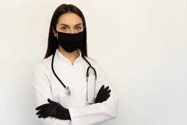 Doctora en máscara médica protectora negra y guantes negros, un estetoscopio en el cuello — Foto de Stock