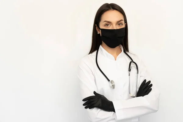 Siyah koruyucu maskeli ve siyah eldivenli kadın doktor. Boynunda steteskop var.