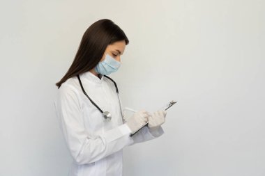 Koruyucu maske ve eldiven takmış kadın doktor, tanıyı müşteri kartına yazar.