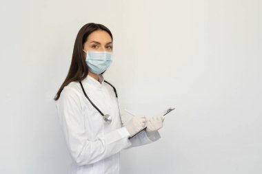 Koruyucu maske ve eldiven takmış kadın doktor, tanıyı müşteri kartına yazar.