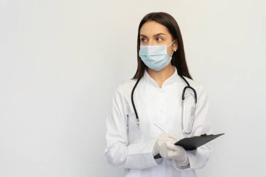 Koruyucu maske ve eldiven takmış kadın doktor, tanıyı müşteri kartına yazar.