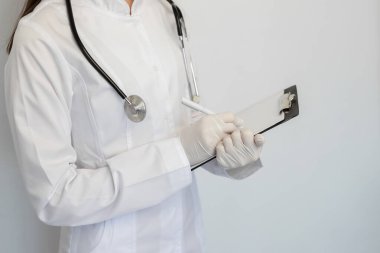 Koruyucu bir maske ve eldiven takmış kadın doktor, tanıyı müşteri kartına yazar.