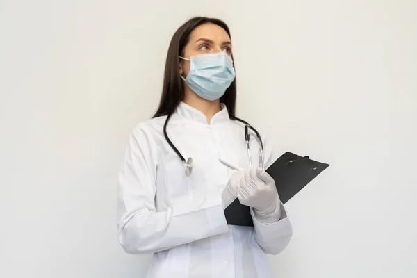 Koruyucu bir maske ve eldiven takmış kadın doktor, tanıyı müşteri kartına yazar.
