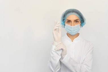 Tıbbi maskeli bir kadın doktor beyaz lastik eldiven takıyor.