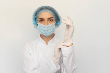 Tıbbi maskeli bir kadın doktor beyaz lastik eldiven takıyor.