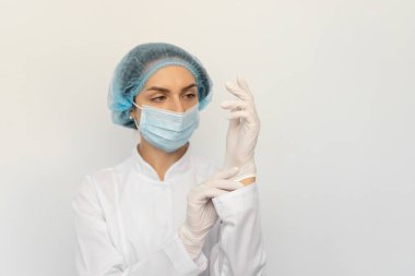 Tıbbi maskeli bir kadın doktor beyaz lastik eldiven takıyor.