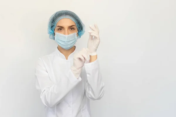 Tıbbi maskeli bir kadın doktor beyaz lastik eldiven takıyor.